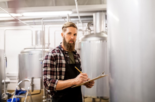 concept de fabrication, d'entreprise et de personnes - homme avec presse-papiers travaillant dans une brasserie artisanale ou une usine de bière