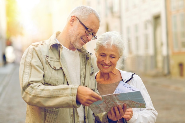 concept de famille, d'âge, de tourisme, de voyage et de personnes - couple de personnes âgées avec carte et guide de la ville dans la rue