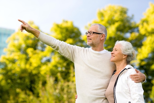 concept de famille, d'âge, de tourisme, de voyage et de personnes - couple de personnes âgées étreignant et pointant le doigt dans le parc