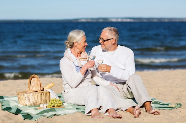 concept de famille, d'âge, de vacances, de loisirs et de personnes - couple de personnes âgées heureux avec panier de pique-nique assis sur une couverture sur la plage d'été