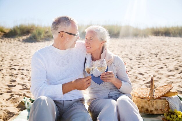 concept de famille, d'âge, de voyage, de tourisme et de personnes - couple de personnes âgées heureux pique-niquer et parler sur la plage d'été