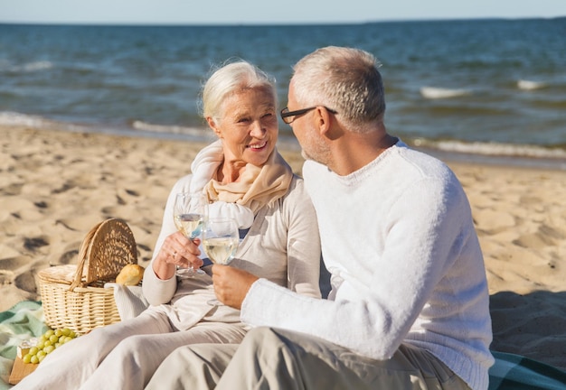 concept de famille, d'âge, de voyage, de tourisme et de personnes - couple de personnes âgées heureux pique-niquer et parler sur la plage d'été