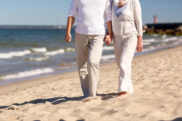 concept de famille, d'âge, de voyage, de tourisme et de personnes - gros plan d'un couple de personnes âgées marchant sur la plage d'été