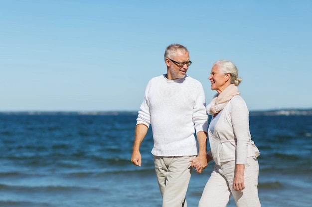 concept de famille, d'âge, de voyage, de tourisme et de personnes - heureux couple de personnes âgées se tenant la main et marchant sur la plage d'été