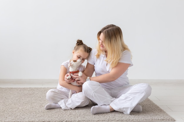 Concept de famille et d'animaux de compagnie - mère et enfant fille assise sur le sol avec chiot Jack Russell Terrier sur fond de salle blanche