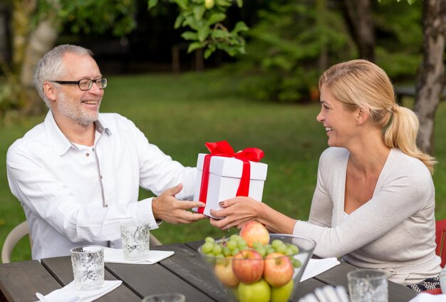 concept de famille, de bonheur, de génération, de maison et de personnes - famille heureuse avec boîte-cadeau en train de dîner en plein air