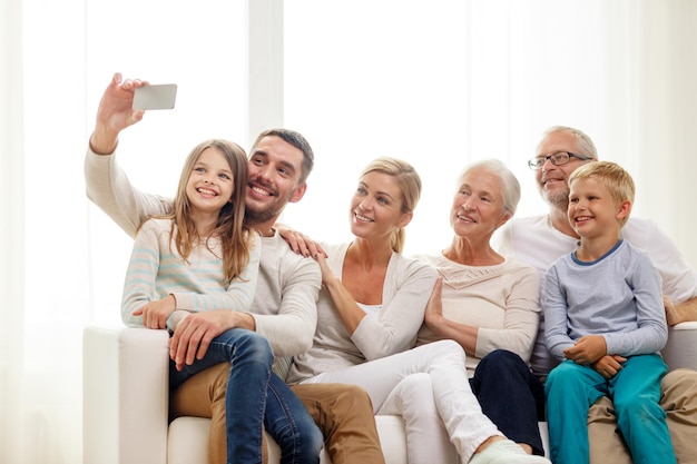 concept de famille, de bonheur, de génération et de personnes - famille heureuse assise sur un canapé et faisant du selfie avec un smartphone à la maison