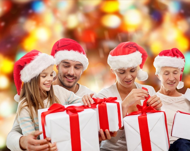 concept de famille, de bonheur, de génération, de vacances et de personnes - famille heureuse en chapeaux de santa helper avec coffrets cadeaux assis sur un canapé sur fond de feux rouges