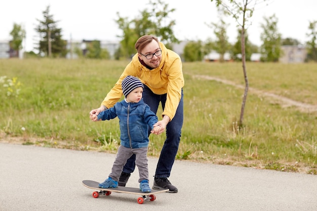 concept de famille, d'enfance, de paternité, de loisirs et de personnes - un père heureux apprend à son petit fils à faire du skateboard