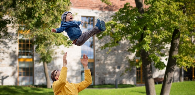 concept de famille, d'enfance, de paternité, de loisirs et de personnes - père heureux et petit fils jouant et s'amusant à l'extérieur sur fond de cour de ville d'été