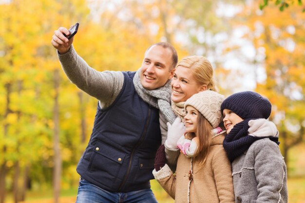 concept de famille, d'enfance, de saison, de technologie et de personnes - famille heureuse prenant selfie avec smartphone dans le parc d'automne