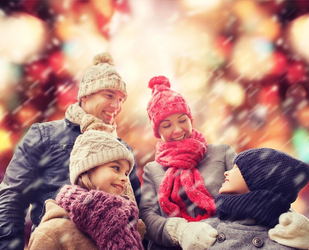 Photo concept de famille, d'enfance, de saison, de vacances et de personnes - famille heureuse en vêtements d'hiver sur fond de feux rouges et de neige