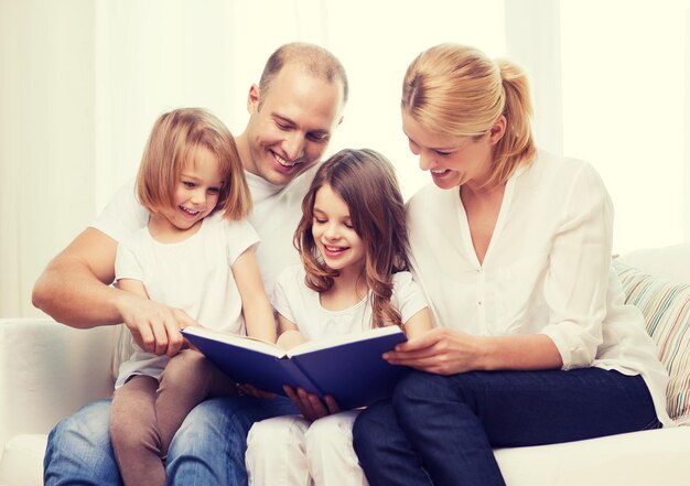 concept de famille, d'enfant et de maison - famille souriante et deux petites filles avec un livre à la maison