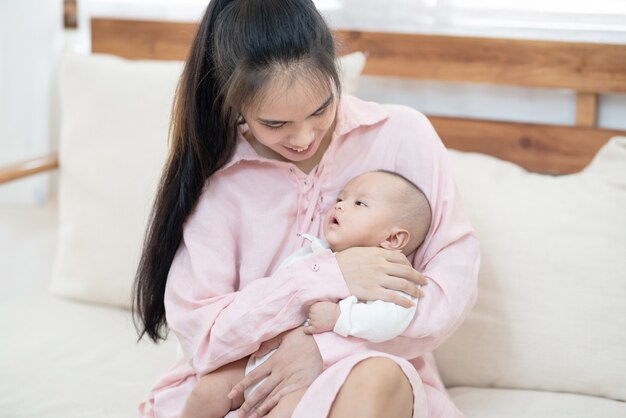 Concept de famille, d'enfant et de parentalité - heureuse belle jeune mère asiatique souriante étreignant tenant le nouveau-né dans ses bras à la maison.