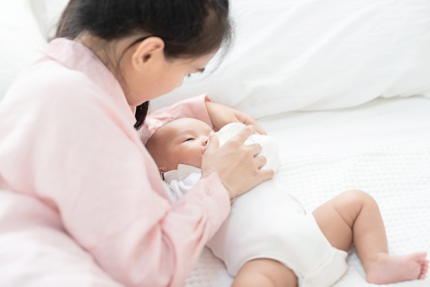 Concept de famille, d'enfant et de parentalité - heureuse belle jeune mère asiatique souriante étreignant tenant le nouveau-né dans ses bras et nourrir le lait sur le lit à la maison.