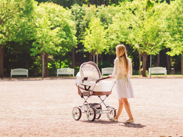 Concept de famille, enfant et parentalité - heureuse mère marchant avec une poussette dans le parc de l'arrière