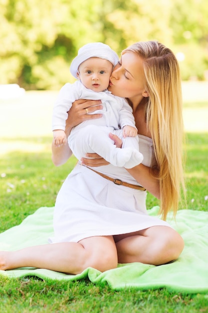 concept de famille, d'enfant et de parentalité - mère heureuse embrassant son petit bébé et assise sur une couverture dans le parc