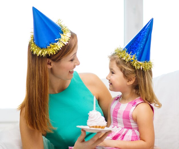 concept de famille, d'enfants, de célébration et de personnes heureuses - heureuse mère et fille en chapeaux de fête bleus avec gâteau et bougie