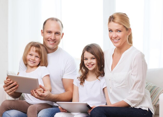 concept de famille, d'enfants, de technologie, d'argent et de maison - famille souriante et deux petites filles avec des tablettes pc à la maison