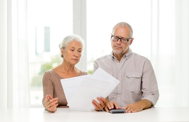 concept de famille, d'entreprise, d'épargne, d'âge et de personnes - couple de personnes âgées avec papiers et calculatrice à la maison