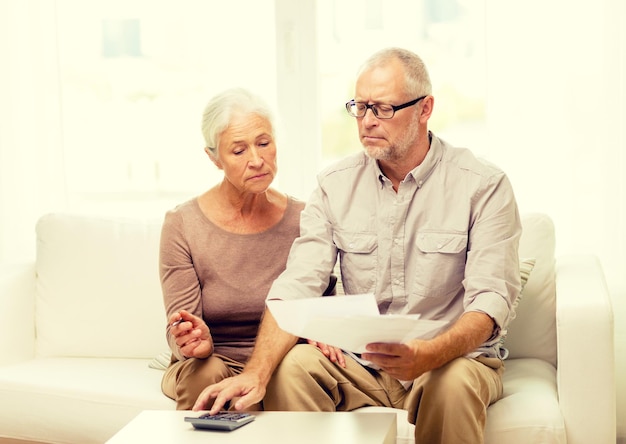 concept de famille, d'entreprise, d'épargne, d'âge et de personnes - couple de personnes âgées souriant avec papiers et calculatrice à la maison