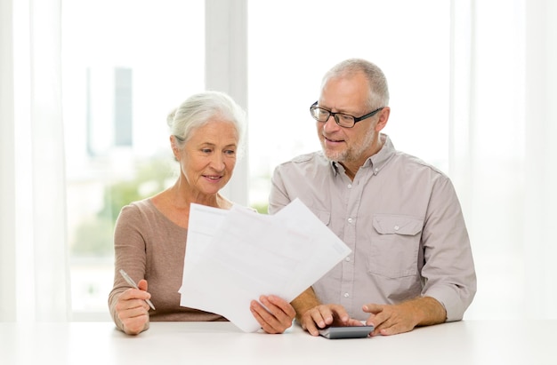 concept de famille, d'entreprise, d'épargne, d'âge et de personnes - couple de personnes âgées souriant avec papiers et calculatrice à la maison