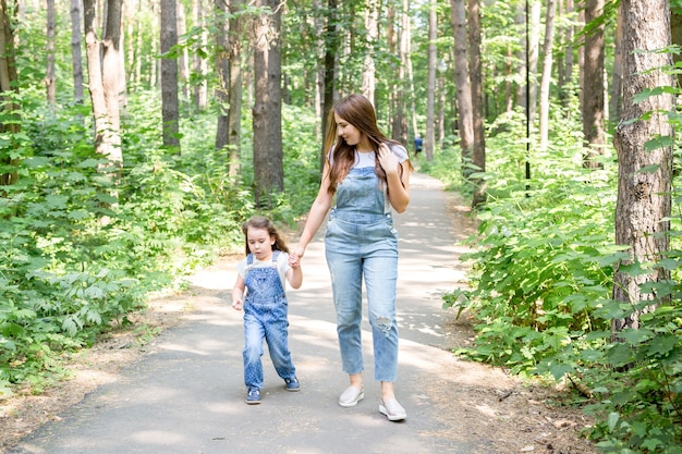 Concept de famille, été et nature - jolie jeune femme et belle petite fille fille marchant dans un parc verdoyant.