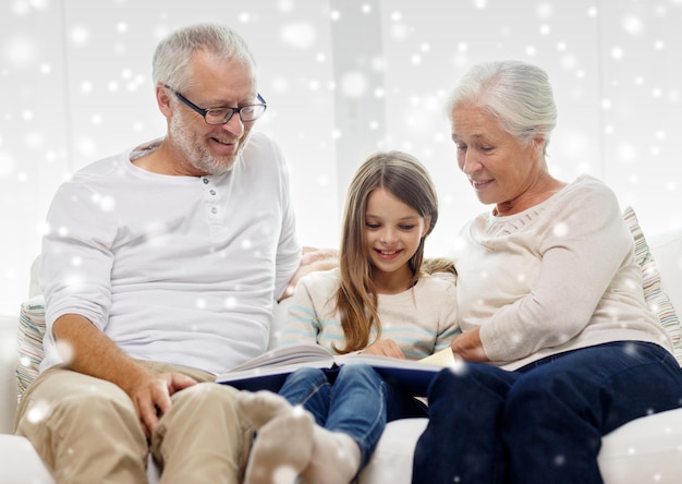 concept de famille, de génération, d'éducation et de personnes - grand-père, petite-fille et grand-mère souriants avec un livre ou un album photo assis sur un canapé à la maison