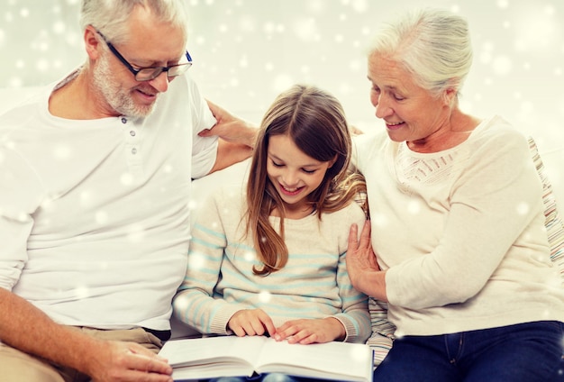 concept de famille, de génération, d'éducation et de personnes - grand-père, petite-fille et grand-mère souriants avec un livre assis sur un canapé à la maison