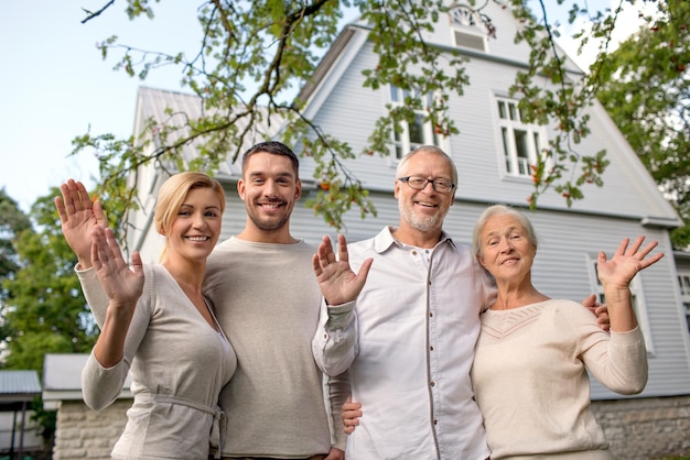 concept de famille, de génération, de maison, de geste et de personnes - famille heureuse debout devant la maison en agitant les mains à l'extérieur