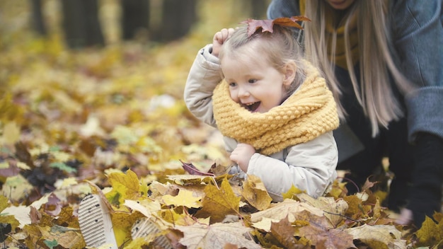 Concept de famille heureuse - petite fille avec sa mère joue avec des feuilles jaunes dans un parc d'automne