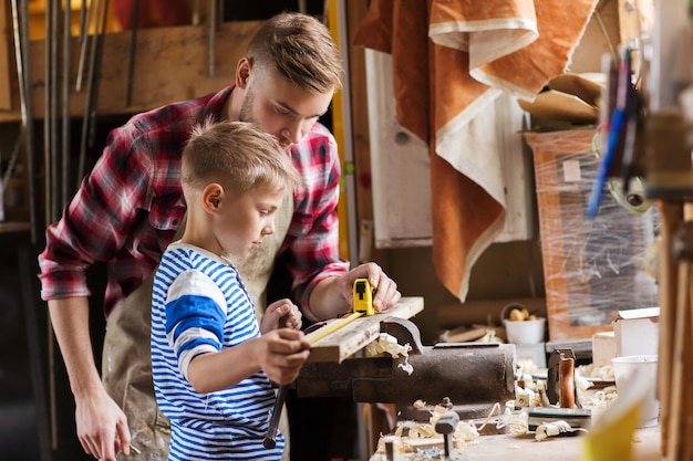 Photo concept de famille, de menuiserie, de menuiserie et de personnes - père et petit fils avec règle et crayon mesurant la planche de bois à l'atelier