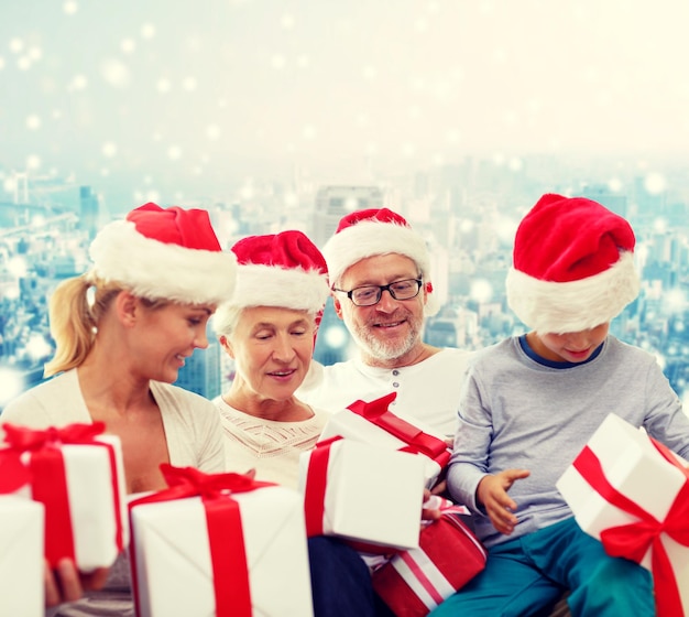 concept de famille, de noël, de génération, de vacances et de personnes - famille heureuse en chapeaux de santa helper avec coffrets cadeaux assis sur fond bleu neigeux