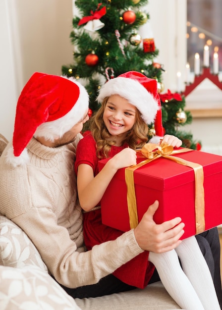 concept de famille, noël, noël, hiver, bonheur et personnes - père et fille souriants dans des chapeaux d'aide santa ouvrant une boîte-cadeau