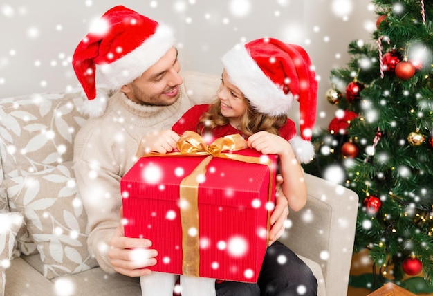 concept de famille, noël, noël, hiver, bonheur et personnes - père et fille souriants dans des chapeaux d'aide santa ouvrant une boîte-cadeau