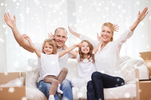 concept de famille, de personnes, d'hébergement, de geste et de bonheur - parents souriants et deux petites filles emménageant dans une nouvelle maison et agitant les mains sur fond de flocons de neige