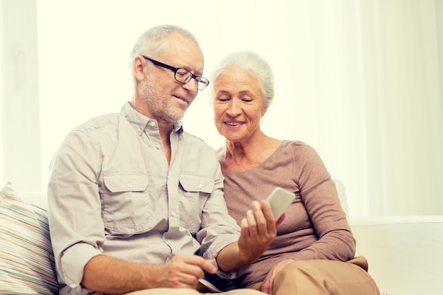 concept de famille, de technologie, d'âge et de personnes - couple de personnes âgées heureux avec smartphone à la maison