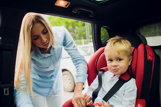 Concept de famille, de transport, de voyage sur la route et de personnes - femme heureuse, attacher l'enfant avec la ceinture de sécurité en voiture