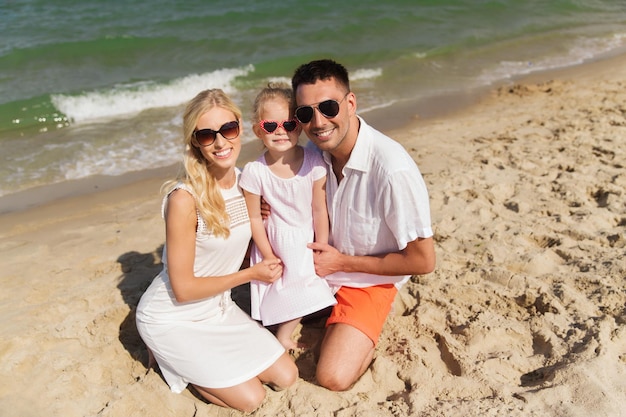 concept de famille, de vacances, d'adoption et de personnes - homme heureux, femme et petite fille à lunettes de soleil sur la plage d'été