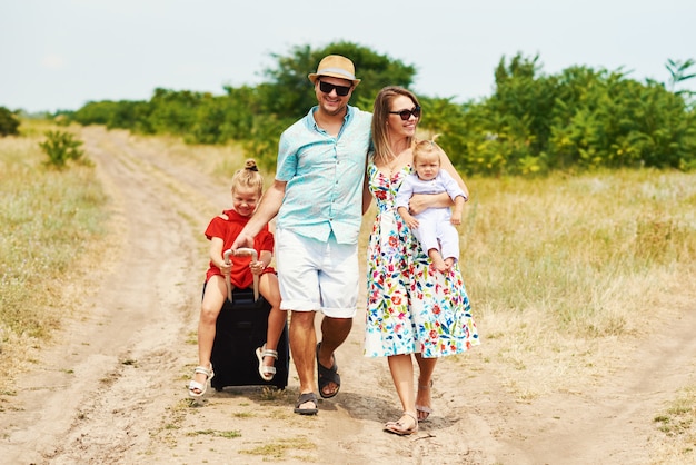 Concept de famille, vacances d'été, adoption et personnes - homme heureux, femme et filles à lunettes de soleil, avec des valises s'amusant sur le ciel bleu