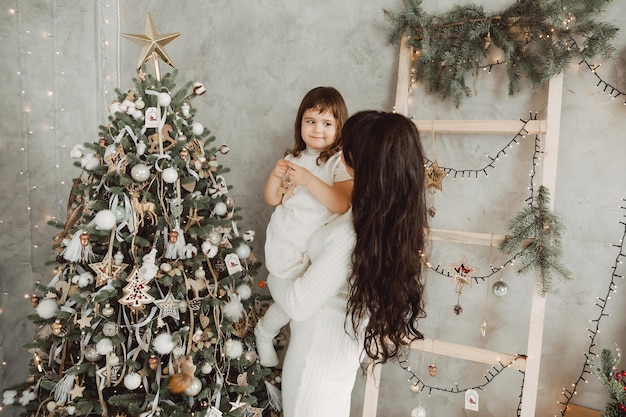 Concept de famille, de vacances d'hiver et de personnes - une mère heureuse tient sa petite fille dans ses bras et décore l'arbre de Noël à la maison