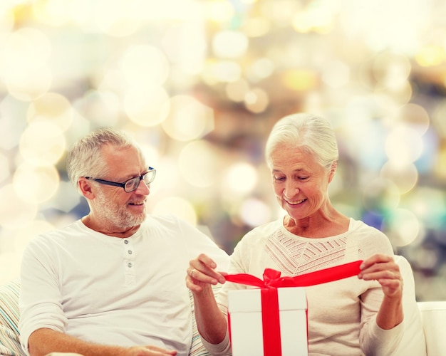 concept de famille, vacances, noël, âge et personnes - couple de personnes âgées heureux avec boîte-cadeau sur fond de lumières