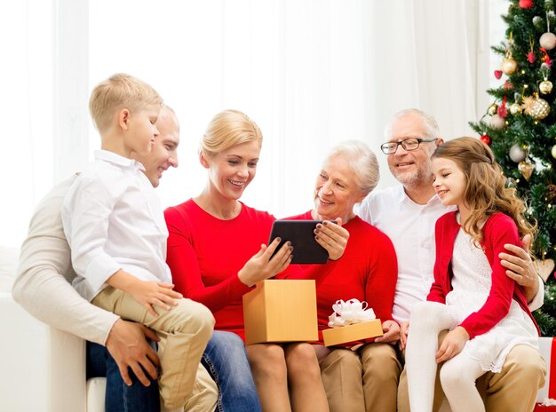 concept de famille, vacances, noël, technologie et personnes - famille souriante avec boîte-cadeau et ordinateur tablette assis sur un canapé à la maison