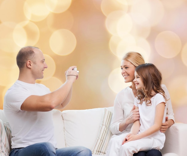 concept de famille, de vacances, de technologie et de personnes - mère souriante, père et petite fille avec caméra sur fond de lumières beiges