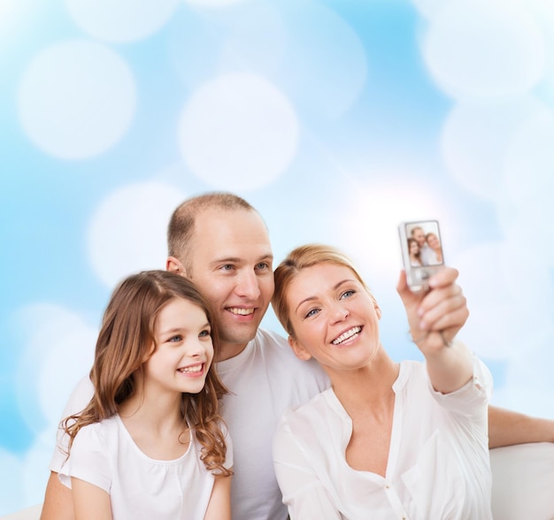 concept de famille, de vacances, de technologie et de personnes - mère souriante, père et petite fille faisant selfie avec caméra sur fond de lumières bleues