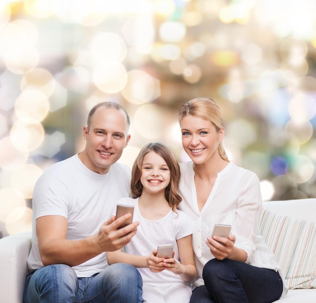 concept de famille, de vacances, de technologie et de personnes - mère souriante, père et petite fille avec des smartphones sur fond de lumières