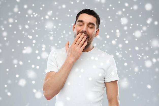 Photo concept de fatigue, d'hiver, de noël et de personnes - homme fatigué qui bâille sur la neige sur fond gris