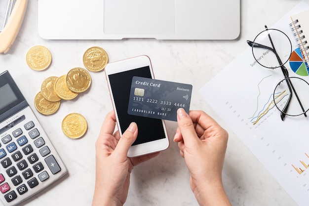 Concept d'une femme faisant le paiement en ligne avec carte et smartphone isolé sur une table de bureau en marbre moderne, maquette, vue de dessus, espace copie, mise à plat, gros plan