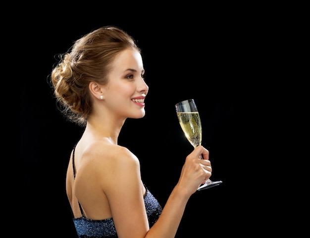 concept de fête, boissons, vacances, luxe et célébration - femme souriante en robe de soirée avec verre de vin mousseux sur fond noir