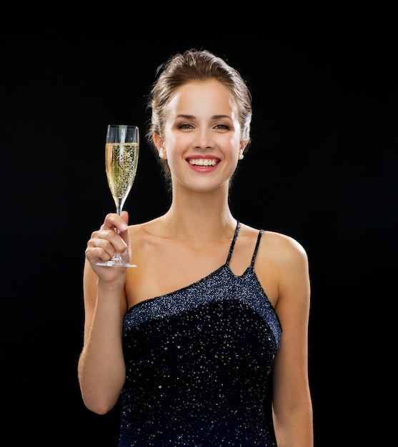 concept de fête, boissons, vacances, luxe et célébration - femme souriante en robe de soirée avec verre de vin mousseux sur fond noir